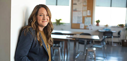 Adult leaning against wall in front of empty classroom